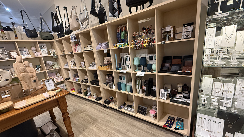 Image of wrap around cubed shelves filled with products from Ruby's Gifts that are perfect for gifting. Handbags hanging off standalone racks on the top of the shelves displayed.