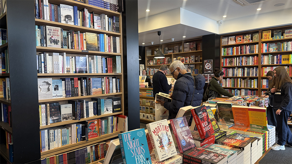 Interior image of Avenue Bookstore in Elsternwick Village, with rows and shelves of colourful books on display with a man with grey hair reading a book with his back turned to the camera.