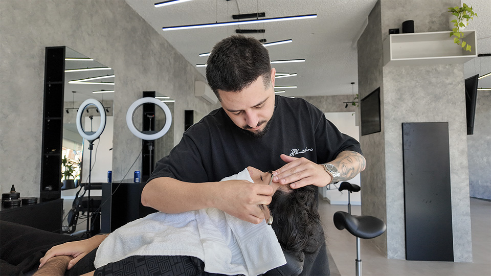 Owner and barber Gian Smalti grooming a client's eyebrows in the salon chair