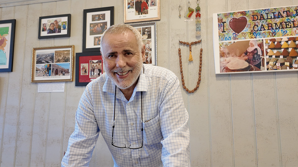 Photo of owner of restaurant Talk of the Town, Ady Maklada, standing in front of a wall full of nostalgic pictures, smiling.
