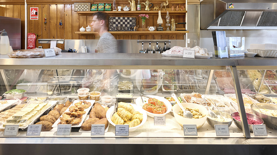 Photo of staff member behind the fridge counter walking in a blur, fridge filled with a huge selection of pre-prepped middle eastern dishes